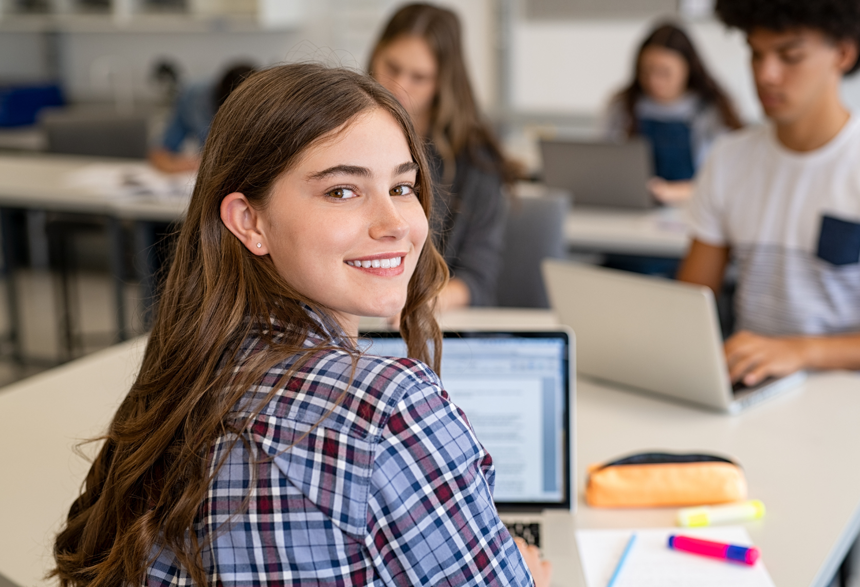 High school student at their desk with a laptop open in front of them and looking back at the camera for a photo. 